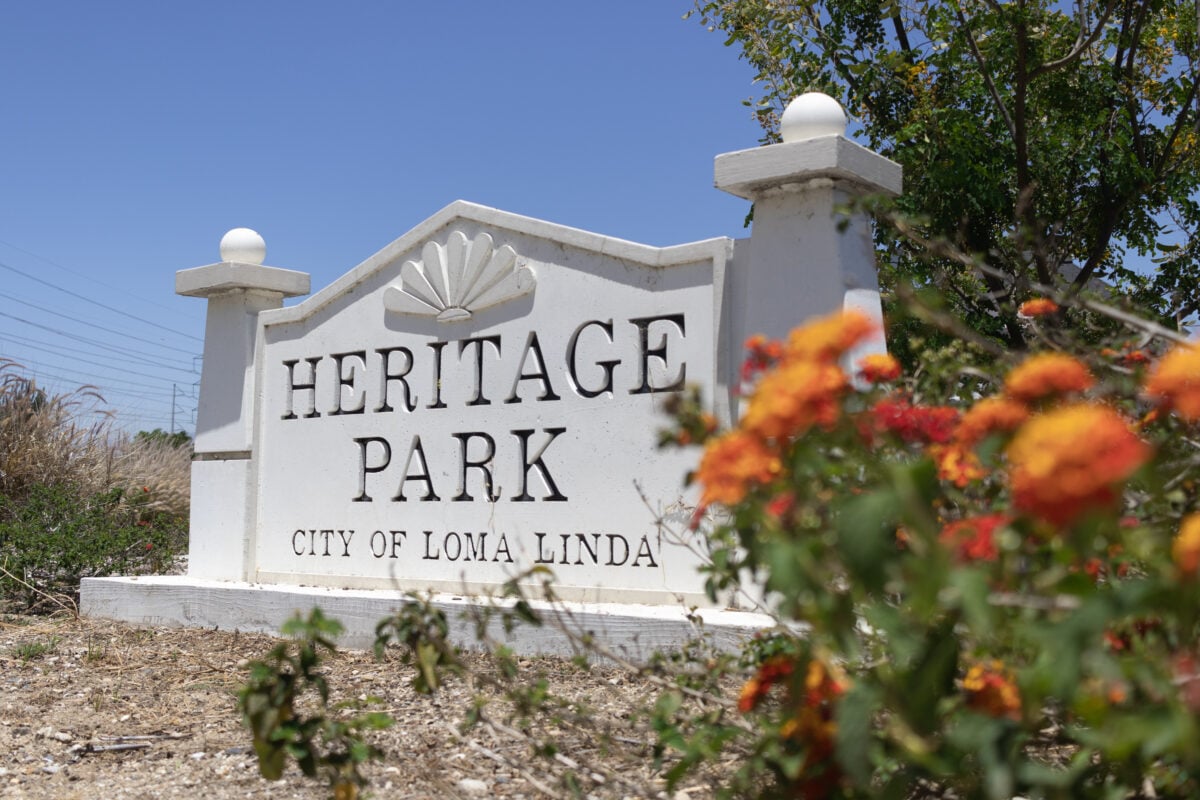 A sign reading "Heritage Park, City of Loma Linda" next to a flower bush, taken in the Blue Zone area of Loma Linda